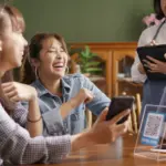 Group of friends laughing and paying together with WOI E money, demonstrating easy split bill features in a white label cashless payment solution