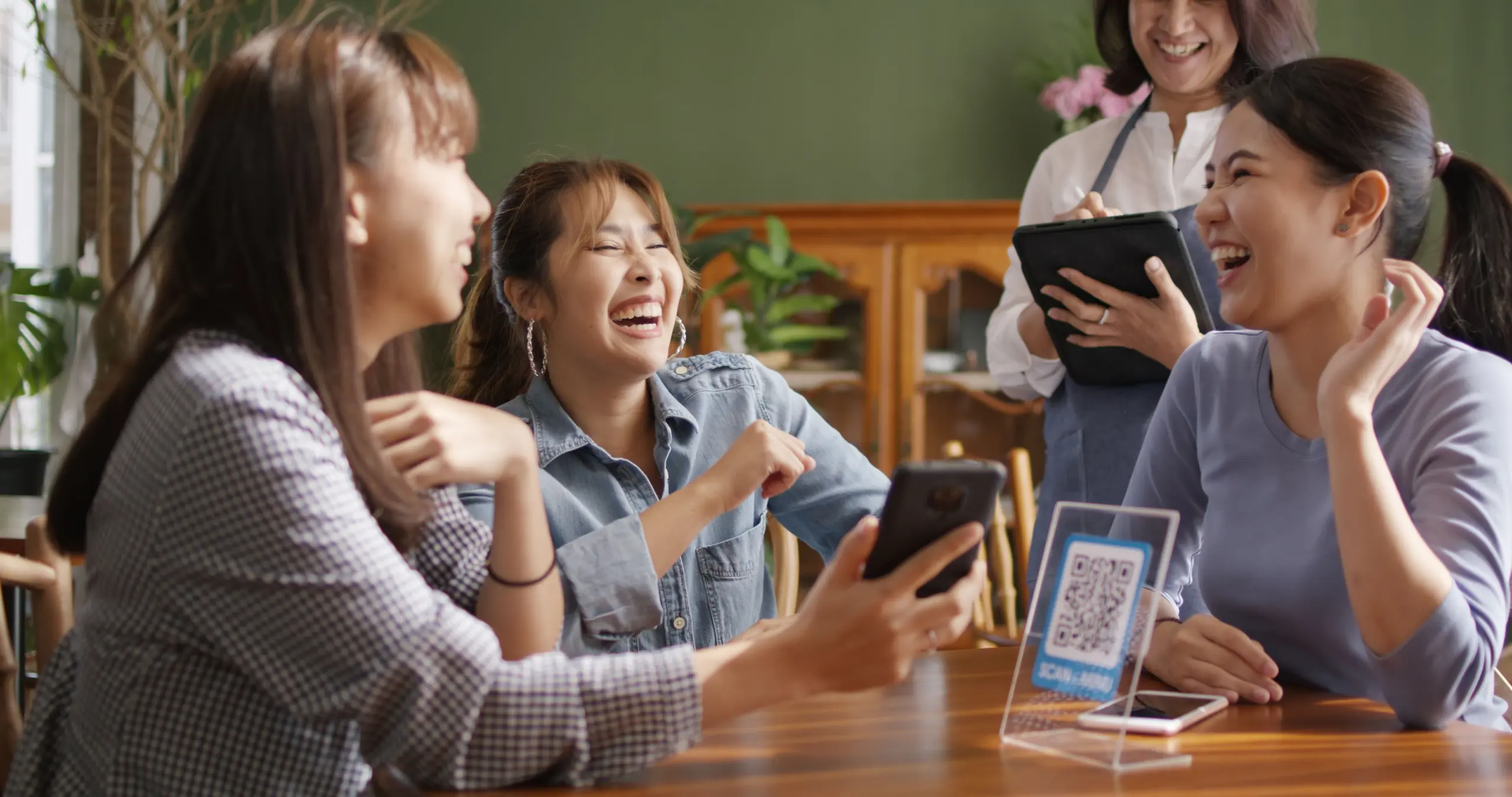 Group of friends laughing and paying together with WOI E money, demonstrating easy split bill features in a white label cashless payment solution